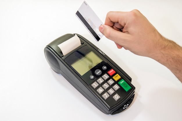 男性の手は、カードマシンのピンパッドまたはピン端子にピンコードをダイヤルし、白い背景に白いクレジットカードが挿入された状態で挿入します。クレジットカードでの支払い -  POS端末を持っているビジネスマン。