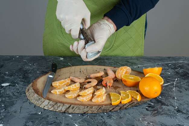 Male hand in gloves adding salt to shrimps on marble table.