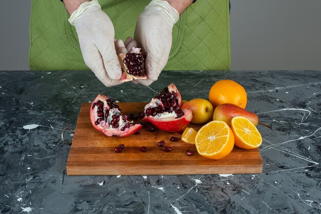 Male hand in gloves breaking red pomegranate on marble table.