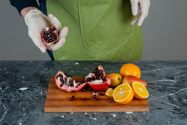 Male hand in gloves breaking red pomegranate on marble table.