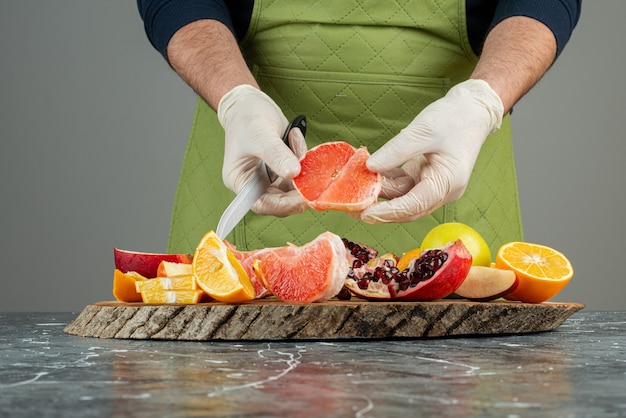 Male hand in gloves cutting juicy grapefruit on marble table.