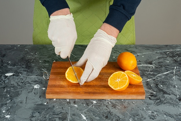 Male hand in gloves cutting juicy orange on marble table.