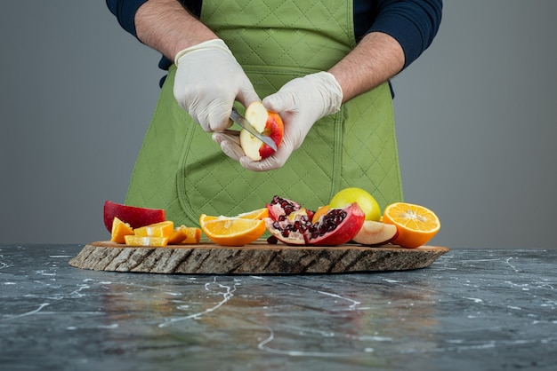 Male hand in gloves cutting red apple on marble table.