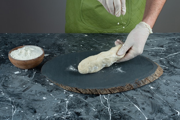 Male hand in gloves making dough on marble table.