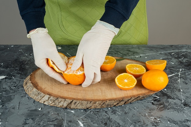 Мужская рука в перчатках, очищающих свежий мандарин на столе.