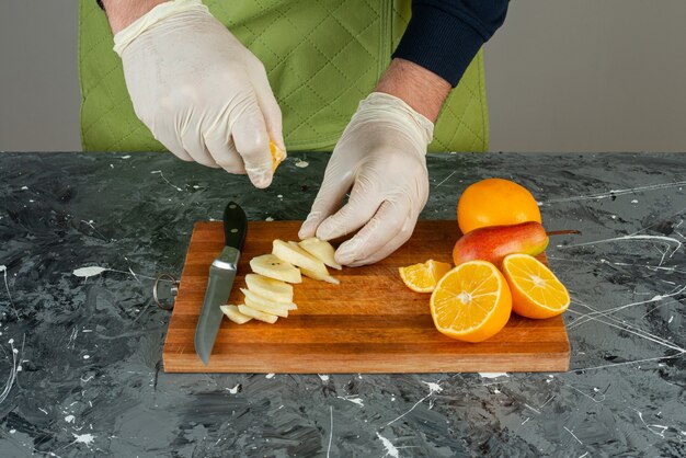 Мужская рука в перчатках, выжимая лимонный сок в яблоки на деревянной доске.