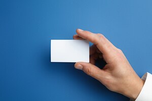 Бесплатное фото Мужская рука держит пустую визитную карточку на синей стене для текста или дизайна. пустые шаблоны кредитных карт для связи или использования в бизнесе. финансы, офис. copyspace.