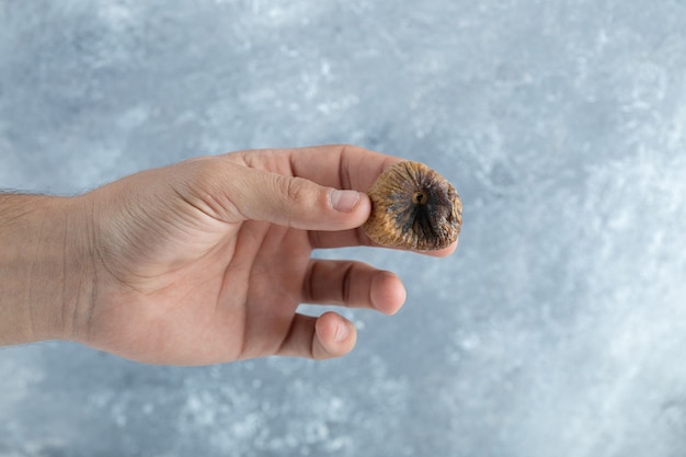 Male hand holding dried fig on marble table. 