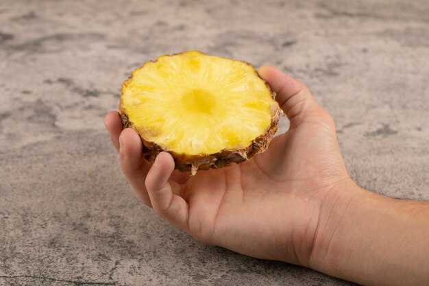 Male hand holding half of pineapple on a stone surface.