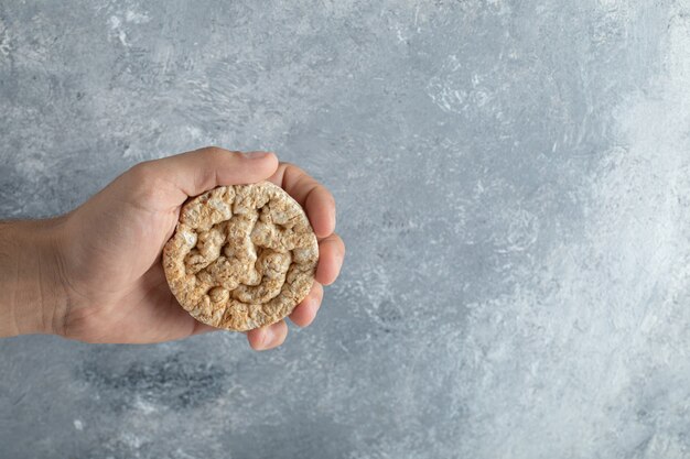 Male hand holding round crispbread on marble surface