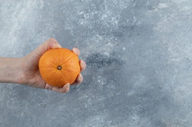 Male hand holding single orange on marble table. 