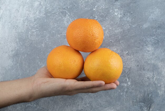 Мужская рука, держащая три апельсина на мраморном столе.