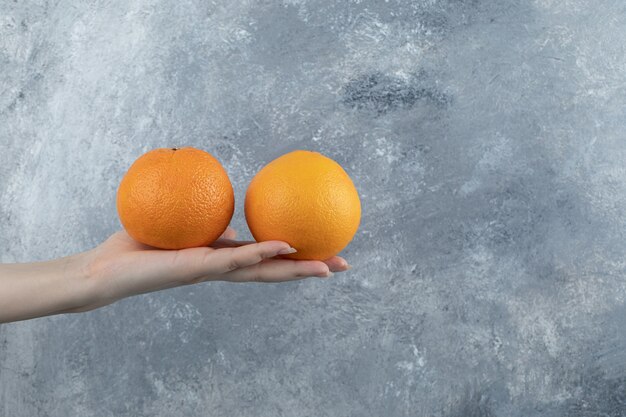 Male hand holding two oranges on marble table.