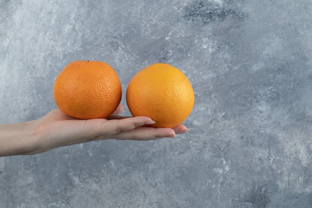 Male hand holding two oranges on marble table. 