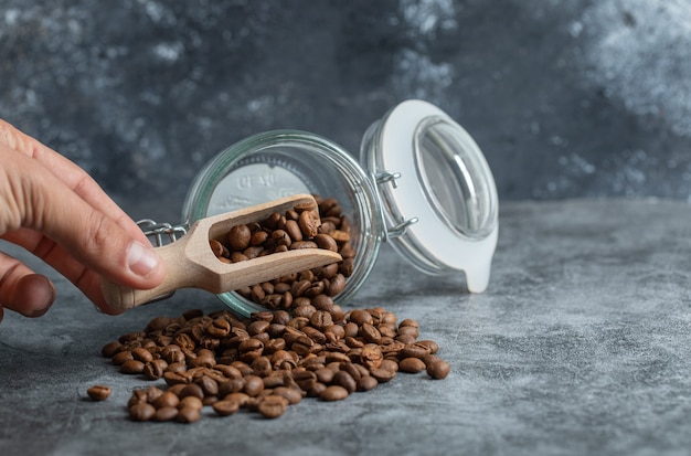 Male hand holding wooden spoon of coffee beans on marble background