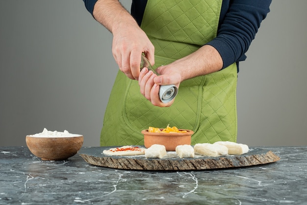 Мужская рука в перчатках, добавляя соль в тесто на мраморном столе.