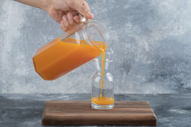 Male hand pouring orange juice into glass.