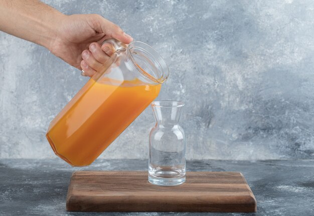 Мужская рука наливает апельсиновый сок в стакан.