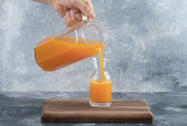 Male hand pouring orange juice into glass. 