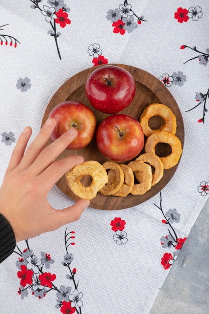 Мужская рука берет кольцо с яблоком из деревянной тарелки.