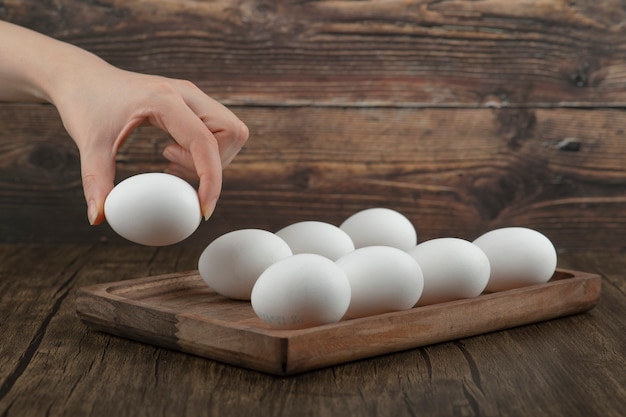 Male hand taking raw organic egg from wooden board.