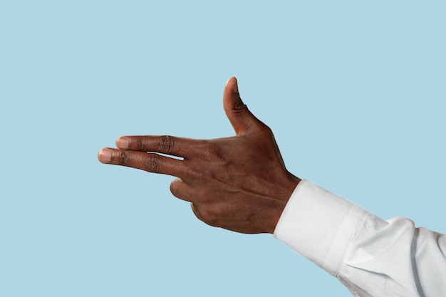 Male hand in white shirt demonstrating a gesture of gun, handgun or pistol isolated on blue  background.