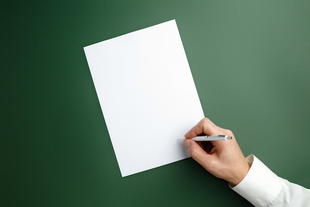 Male hand with a pen and writing on empty sheet on green wall.