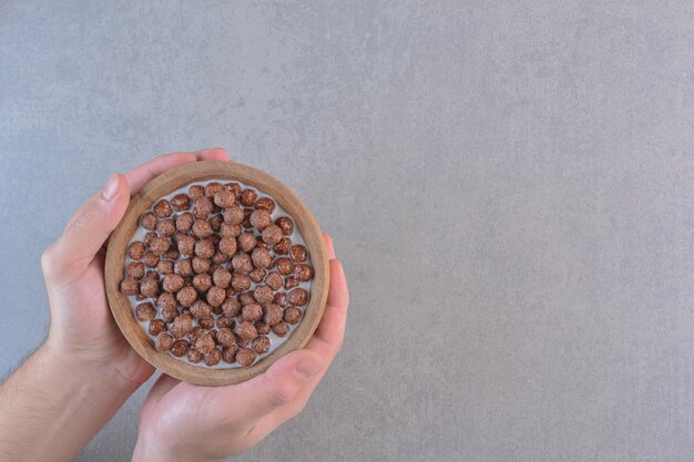 Male hands holding bowl of cereal balls on stone background.