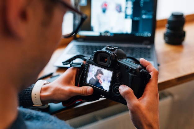 male hands holding professional camera, looks photos, sitting at cafe with laptop.