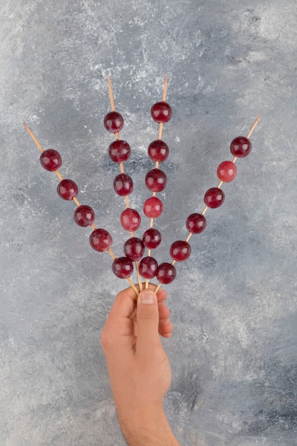 Male hands holding sticks of red grapes on marble surface.