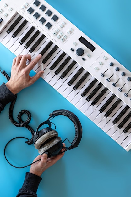 Free photo male hands play musical keys and hold headphones on a blue background top view