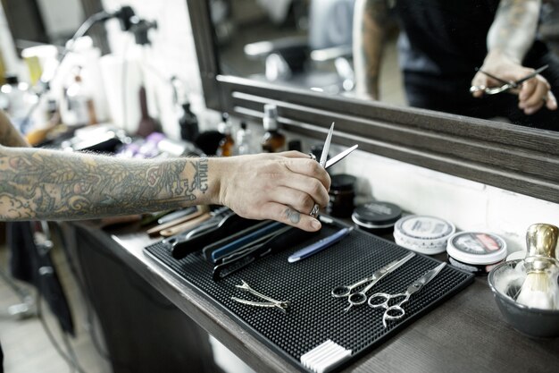 The male hands and tools for cutting beard at barbershop. Vintage tools of barber shop. The hand of the master have tattoo with the word shave