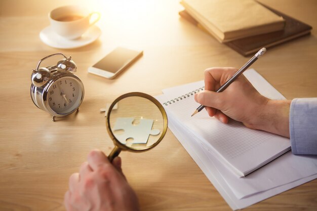 male hands with a pencil and magnifying glass