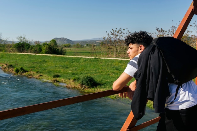 Free photo male hiker leaning on railing looking at idyllic river