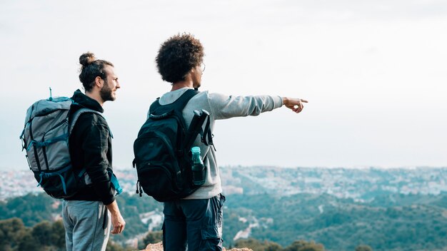 Male hiker looking at african young man pointing finger over the cityscape