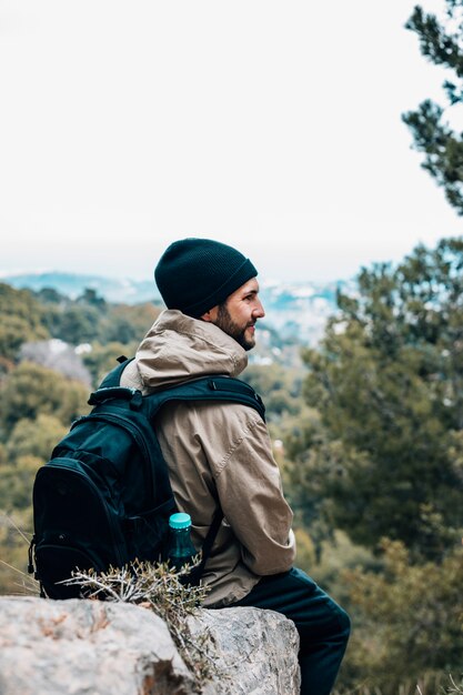A male hiker sitting on rock with his backpack looking at view