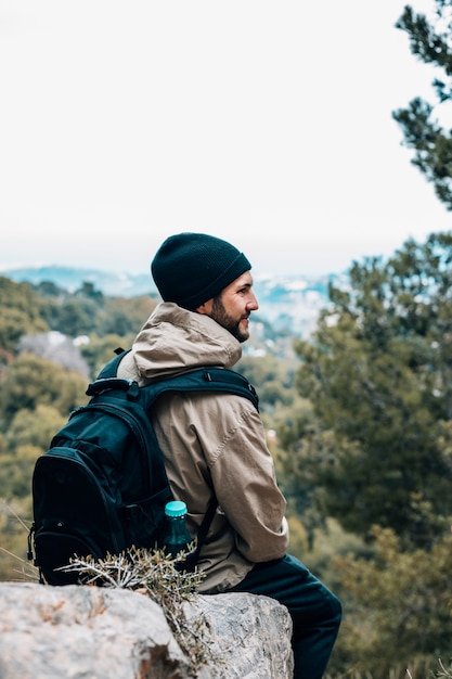 A male hiker sitting on rock with his backpack looking at view
