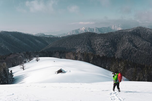 Male hiker taking photos of a winter alpine mountain and a snow covered hut below