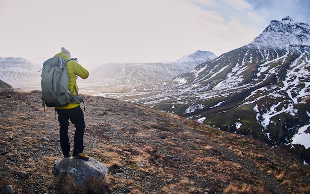 Male hiker with a backpack taking a picture of the rocky mountains covered in the snow