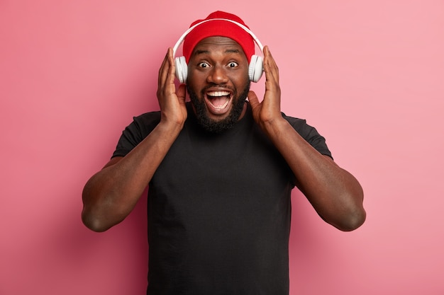 Male hipster listens to music in wireless headphones isolated