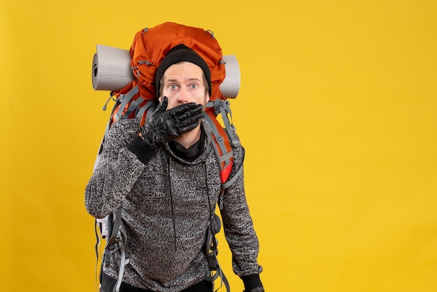 male hitchhiker with leather gloves and backpack covering mouth with hand