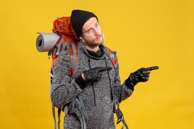 Free photo male hitchhiker with leather gloves and backpack pointing at right