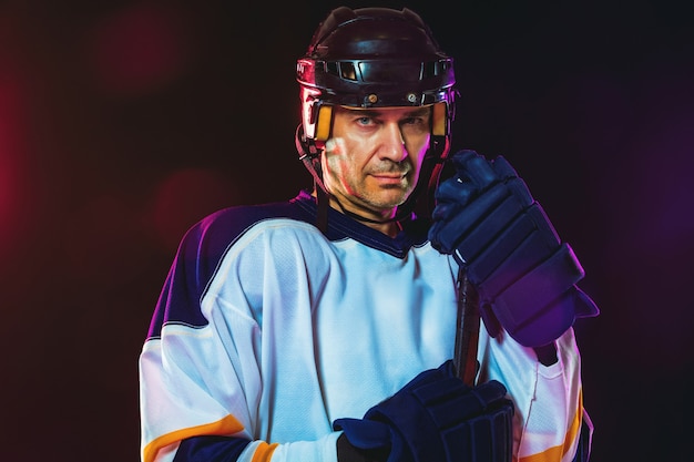 Male hockey player with the stick on ice court and dark neon colored wall