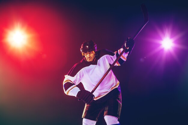 Хоккеист-мужчина с клюшкой на ледовой площадке и стене темного неонового цвета