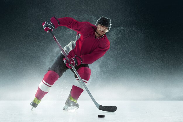 Male hockey player with the stick on ice court and dark wall