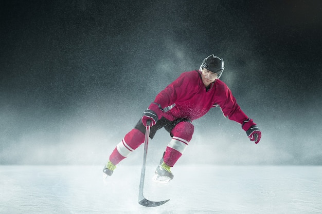 Хоккеист мужского пола с клюшкой на ледовой площадке и темной стене