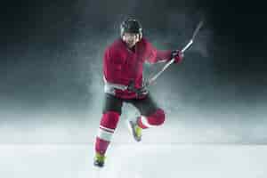 Free photo male hockey player with the stick on ice court and dark wall