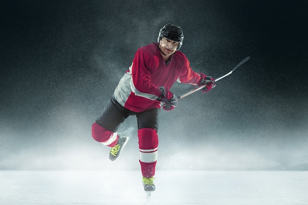 Male hockey player with the stick on ice court and dark wall