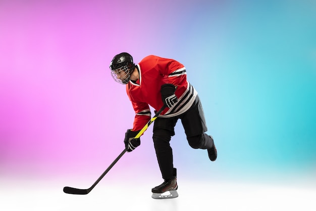 Giocatore di hockey maschio con il bastone sul campo da ghiaccio e sfondo sfumato colorato al neon