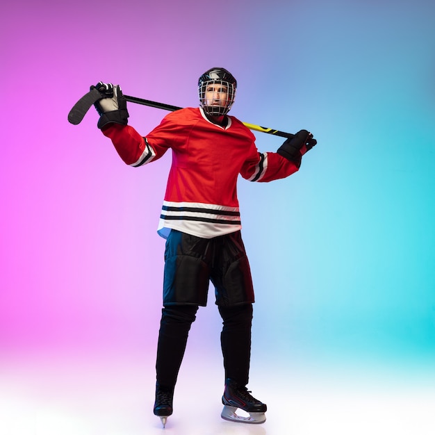 Male hockey player with the stick posing on ice court and neon colored gradient wall